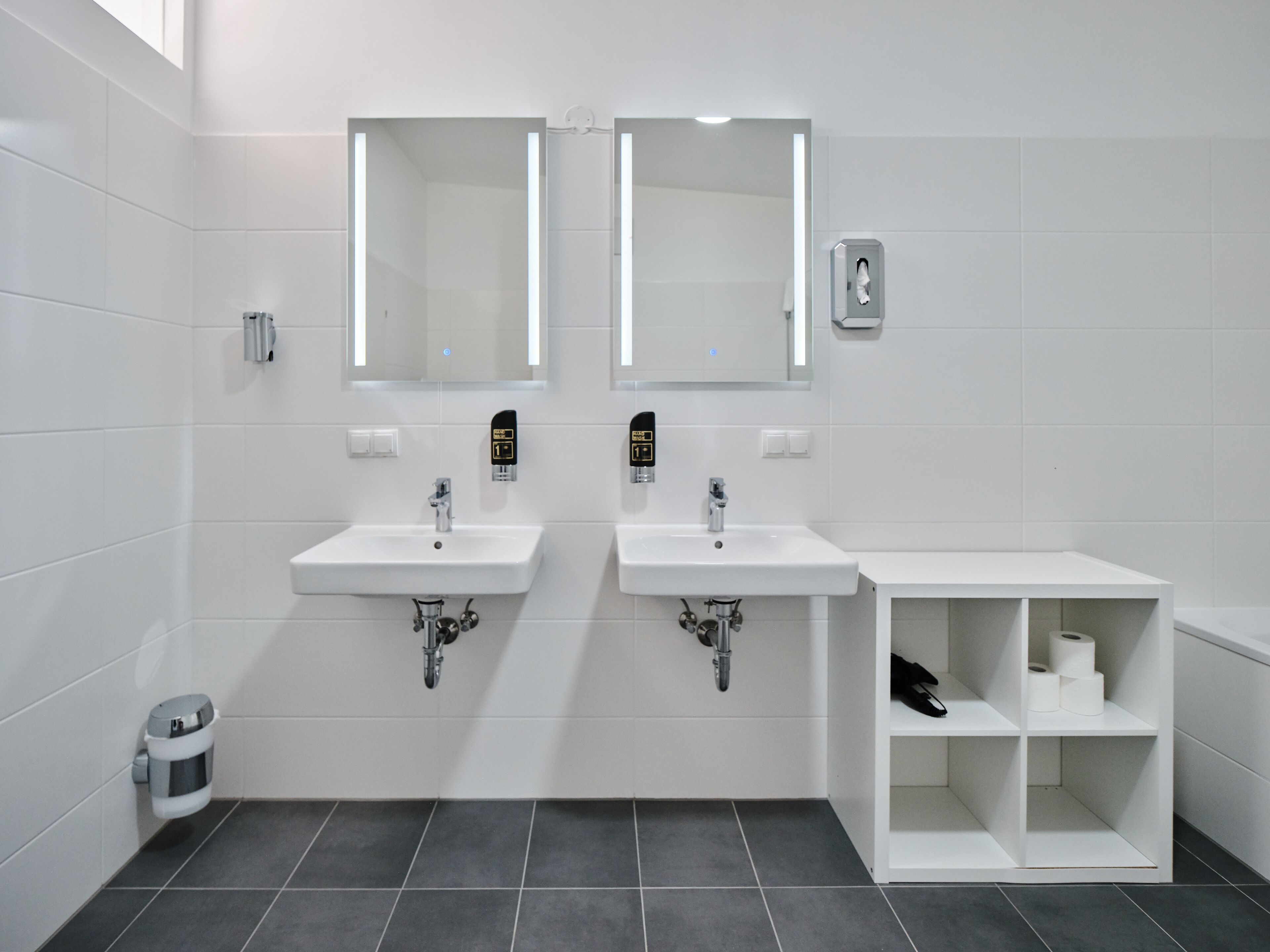 Et moderne badeværelse med to håndvaske, spejle og en hylde med toiletartikler.