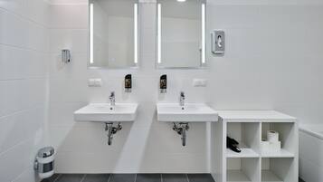 A modern bathroom with two sinks, mirrors, and a shelf with toiletries.