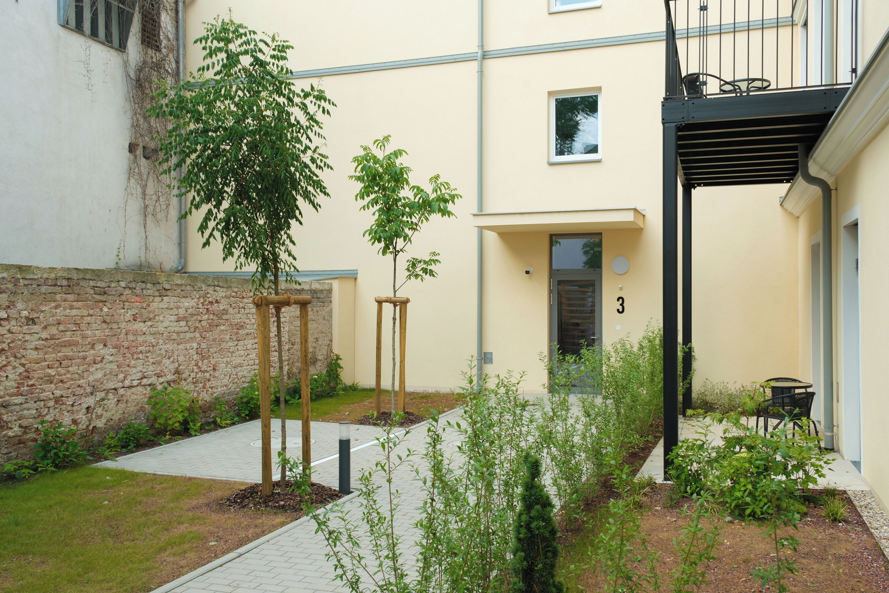 A courtyard with a brick wall, a wooden pergola, and a small garden area with plants and a pathway.