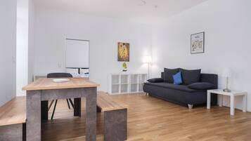 A modern, minimalist living room with a wooden dining table, a grey sofa, and a white side table.