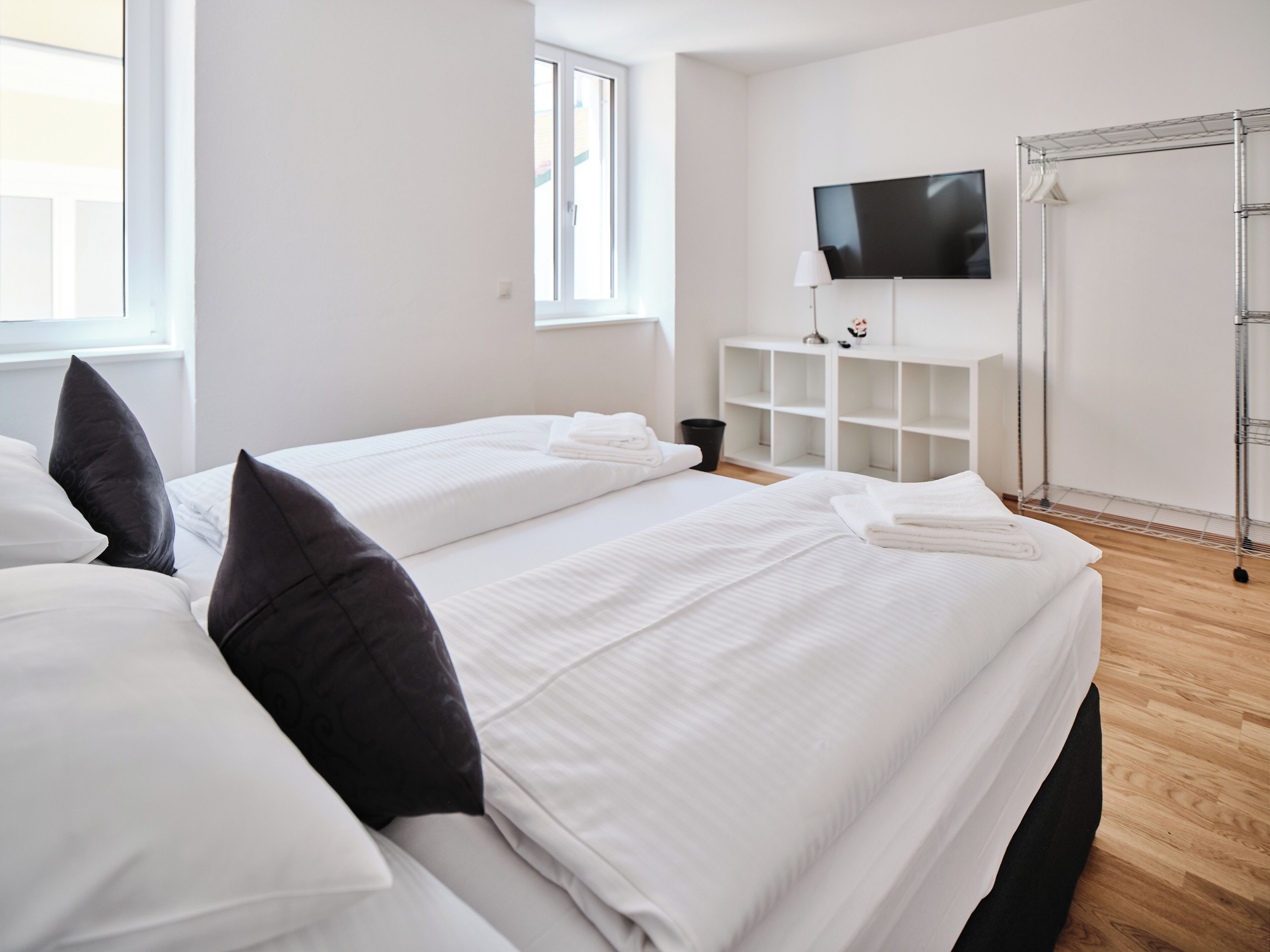 Une chambre d’hôtel avec deux lits, une télévision, une étagère blanche et un étendoir à linge en métal.