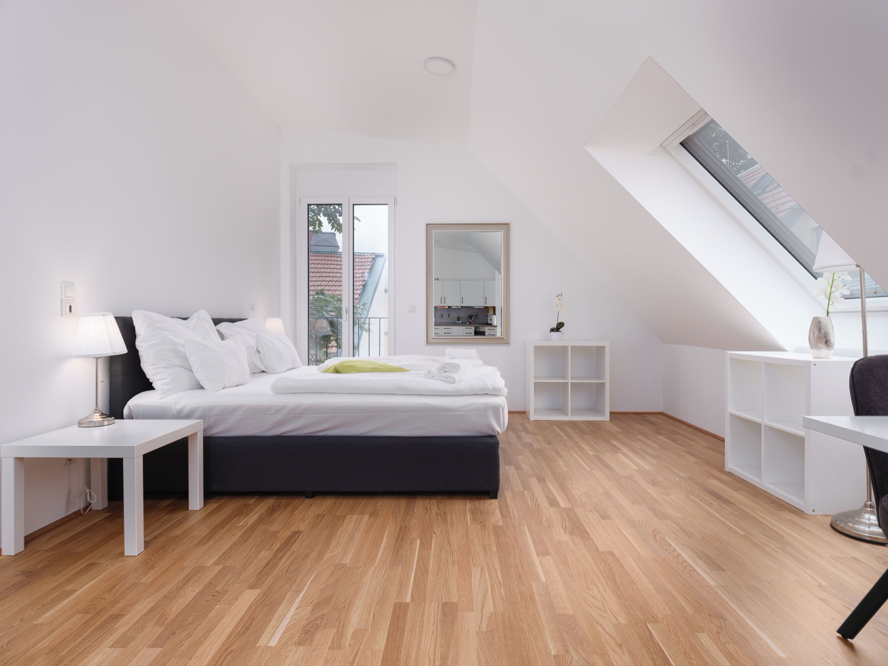 A modern bedroom with a bed, bedside tables, a mirror, and a skylight.