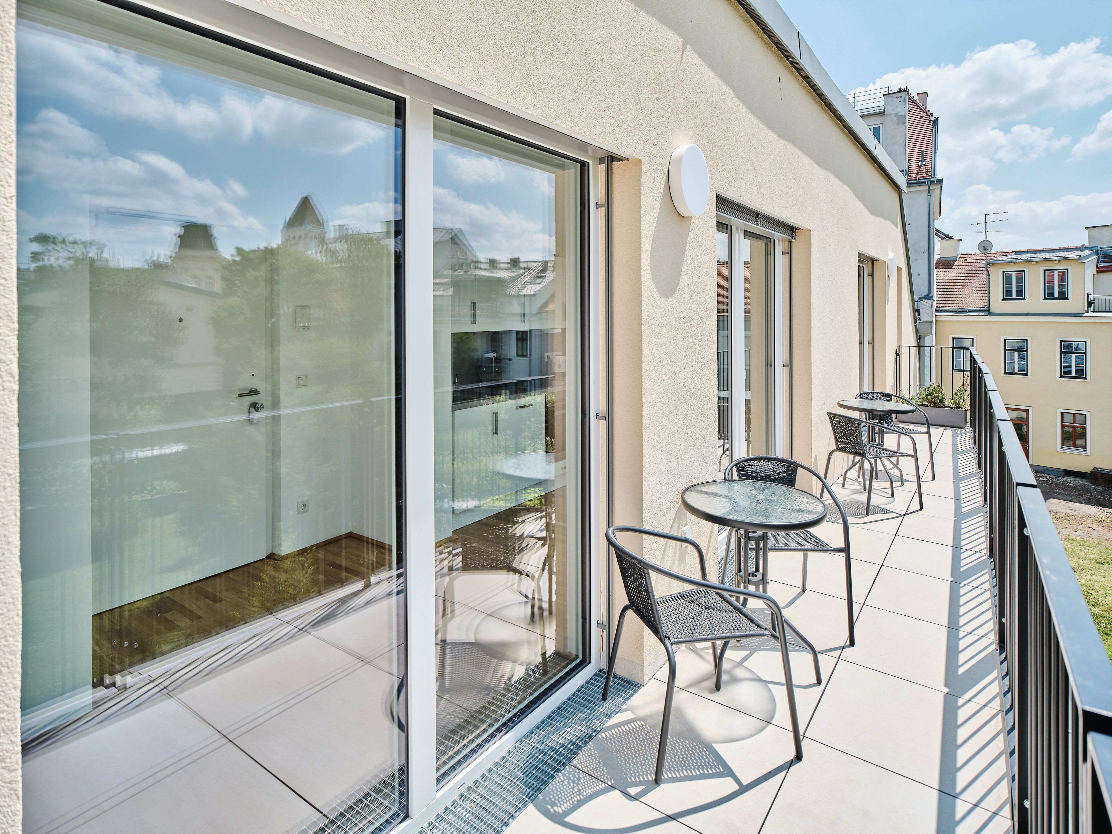 A modern balcony with glass doors, a small table, and two chairs.