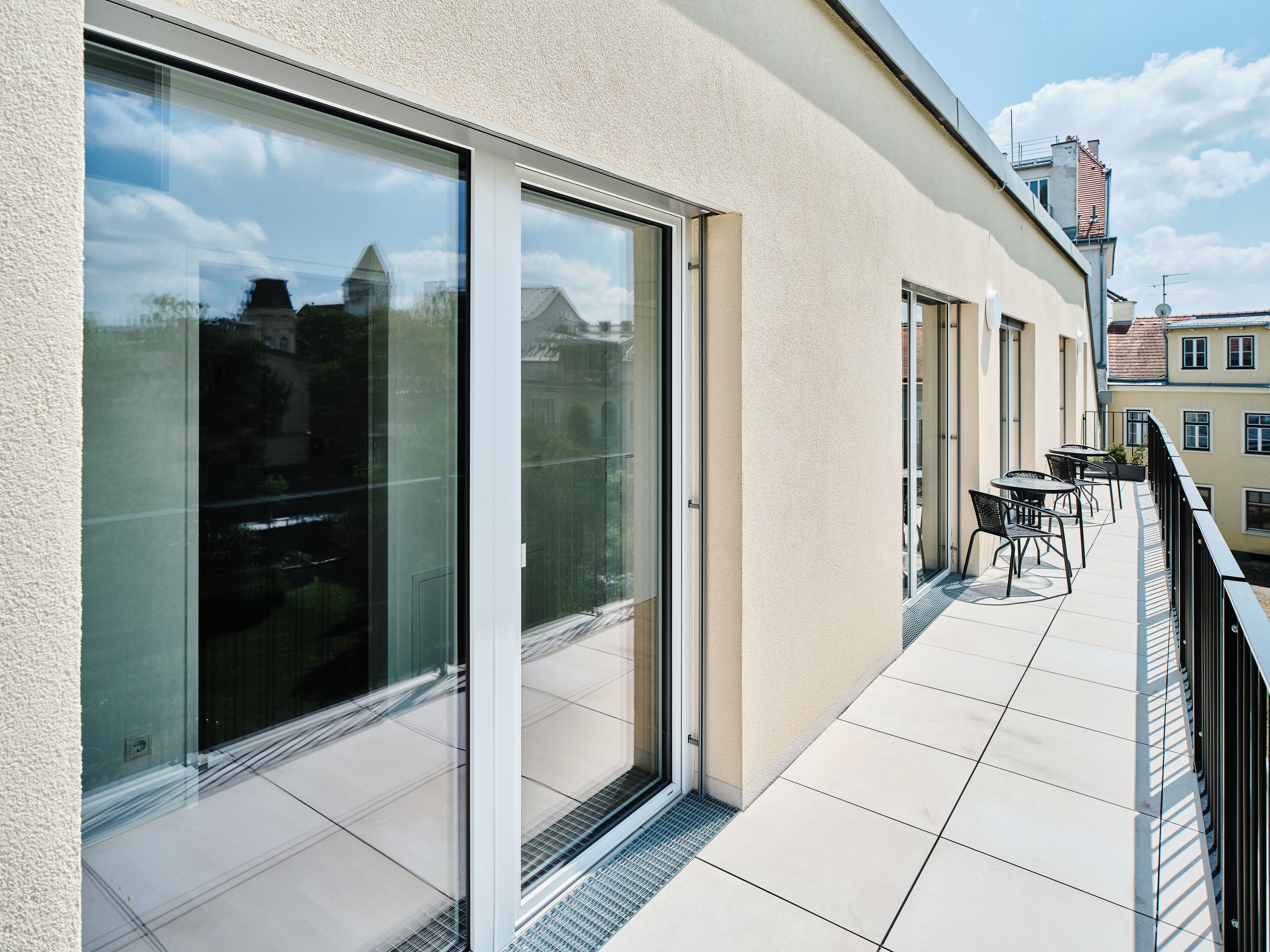 A modern building with large sliding glass doors, a tiled balcony, and a clear view of the sky.