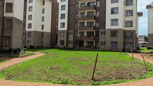 A multi-story residential building with a central courtyard featuring a grassy area and a paved walkway. - Nice 3-bed Apartment in Nairobi (Nairobi)