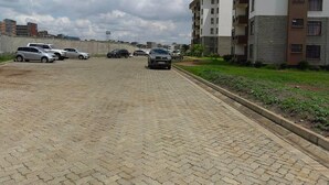 A paved parking area with several cars parked, surrounded by residential buildings with balconies. - Nice 3-bed Apartment in Nairobi (Nairobi)