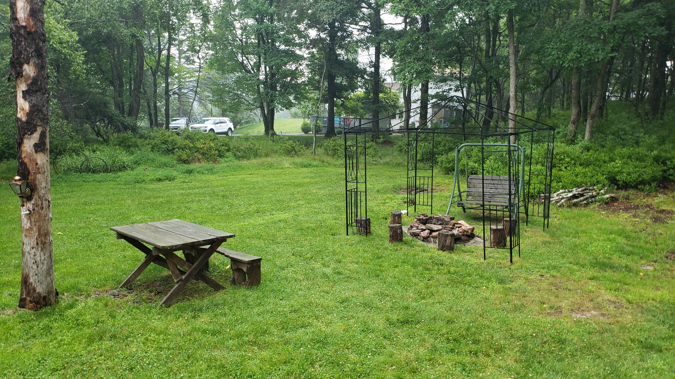A picnic area with a wooden table and benches, surrounded by trees and a swing set.