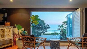 A balcony with wicker chairs, a small table, and a view of the ocean and palm trees. - Tropical beachfront villa in Umdloti - Endless summers (eMdloti)