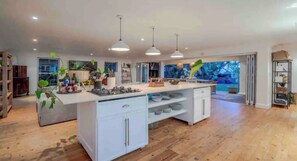 Une cuisine spacieuse dotée d’un îlot central, de luminaires suspendus et offrant une vue sur l’extérieur.