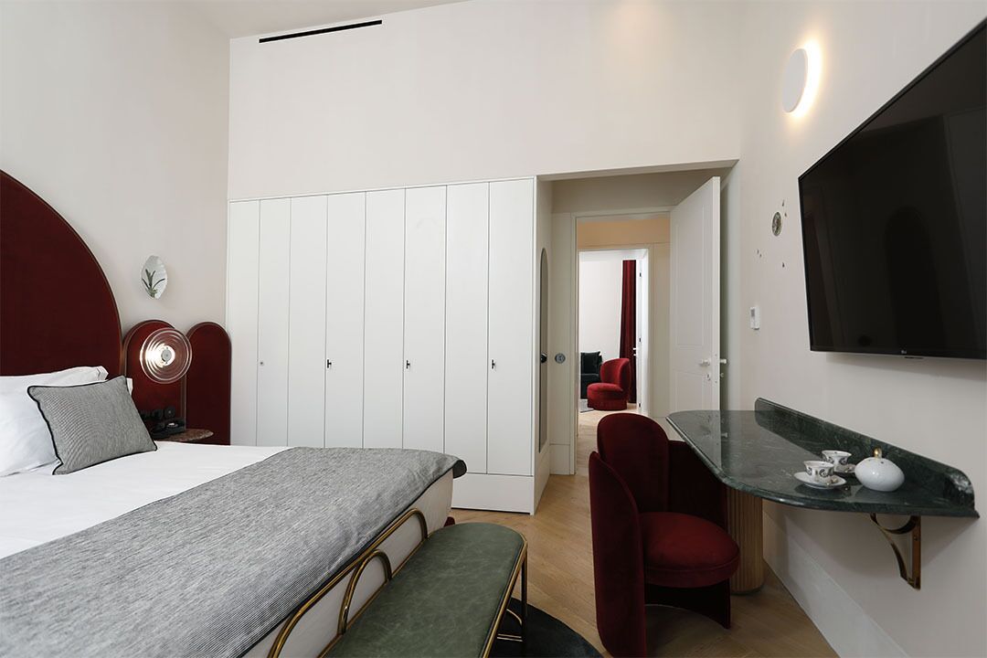 A modern bedroom with a bed, bedside tables, a wardrobe, a desk with a chair, and a TV mounted on the wall.