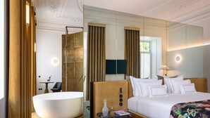A modern hotel room with a large bed, a bathtub, a small table with a vase and a magazine, and a large mirror. - Montebelo Vista Alegre Lisboa Chiado, member of Preferred Hotels & Resorts (Lisbon)
