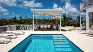Un área de piscina con una pérgola, mobiliario exterior y vistas a la playa.