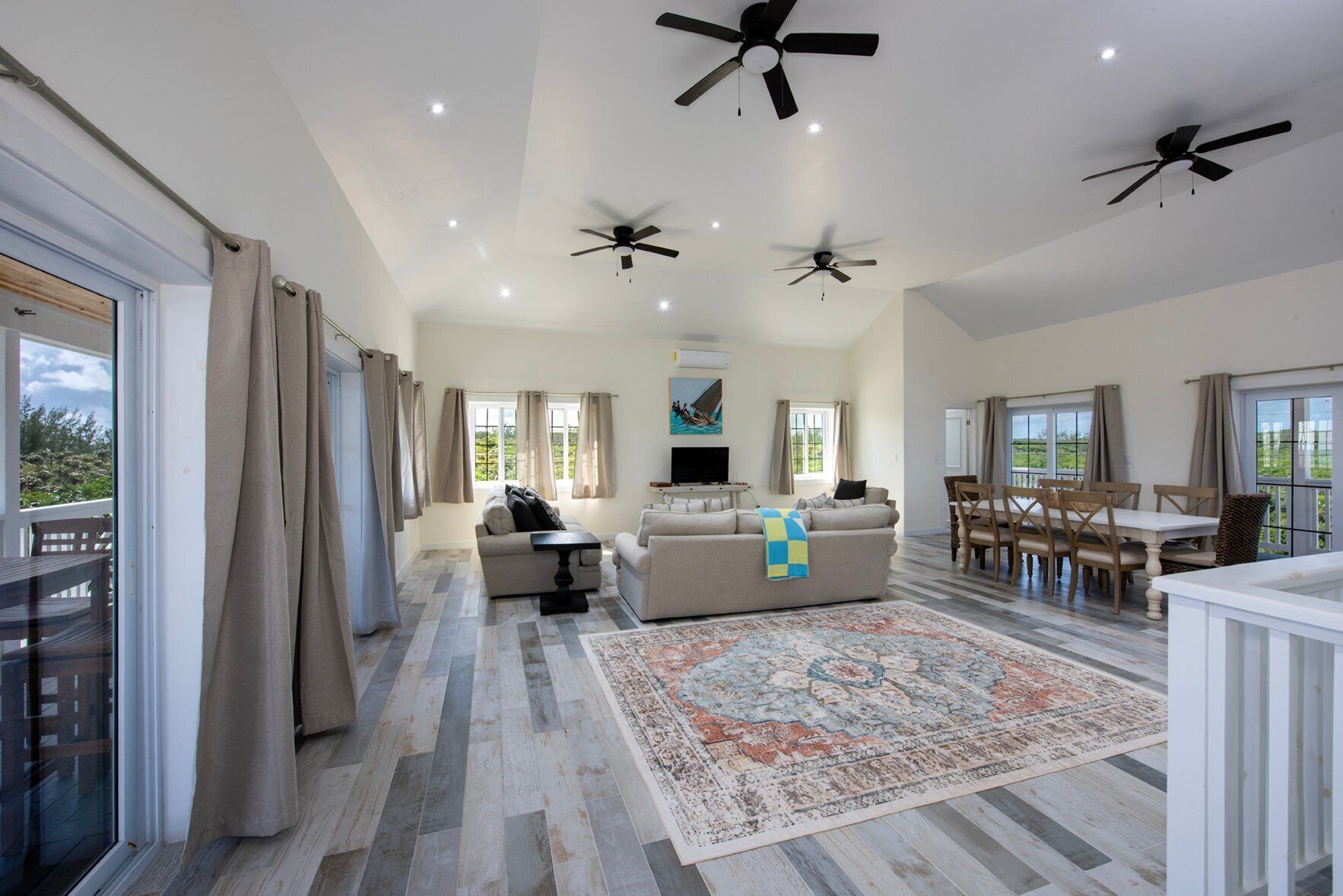 A spacious living area with a large sofa, a dining table, and multiple ceiling fans.