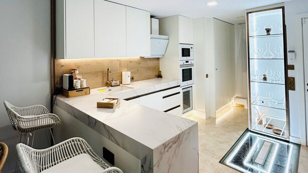 Una cocina moderna con armarios blancos, encimera de mármol y una estantería empotrada para vinos.