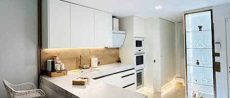Una cocina moderna con armarios blancos, encimera de mármol y una estantería empotrada para vinos.