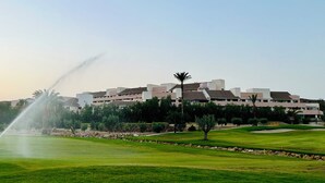 A golf course with a fountain, surrounded by buildings and palm trees. - Apartamento Zen Garden. Valle del Este Golf (AN)