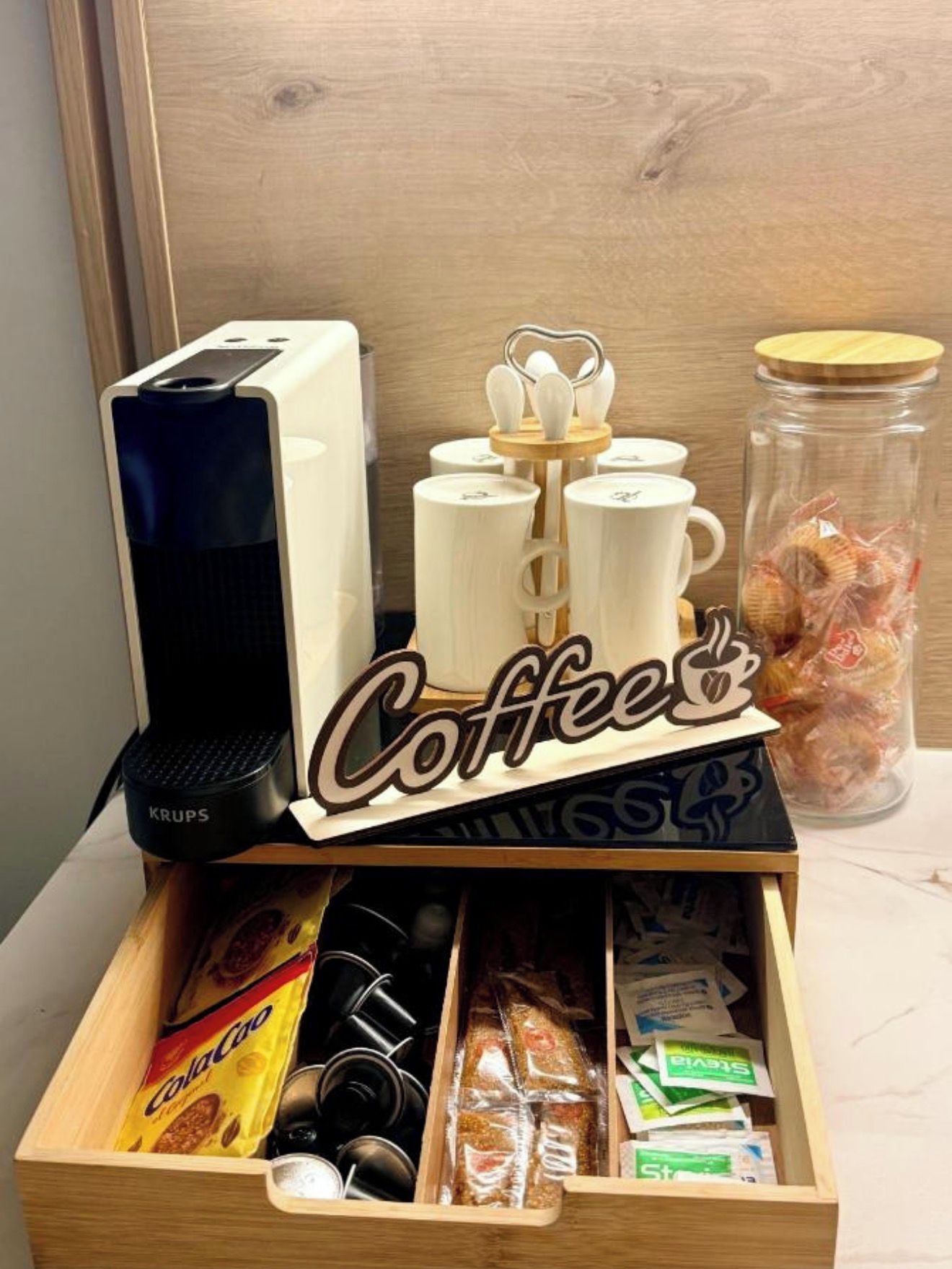 Un coin café équipé d’une machine à café, de tasses et d’un bocal rempli d’en-cas.