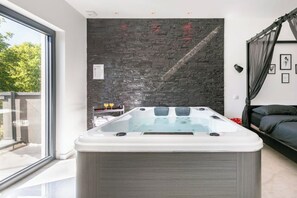 A modern bathroom with a glass-enclosed hot tub, a dark textured wall, and a large window offering a view of greenery. - Meublé 3 Etoiles, Maison Privée, Prox. Strasbourg (Bourgheim)