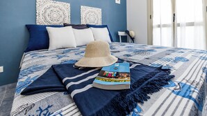 A neatly made bed with a blue and white patterned bedspread, a straw hat, and a book titled "Padrone di Puglia" on the bed.