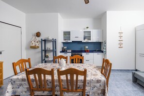 Een kleine keuken met witte kastjes, een blauw aanrecht en een eethoek met houten stoelen en een tafel.
