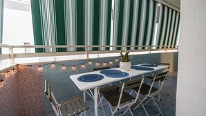 An outdoor dining area with a white table and chairs, a potted plant, and string lights.