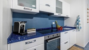 A kitchen with white cabinets, a blue speckled countertop, a coffee maker, a pineapple, and a small plant on the upper cabinets.