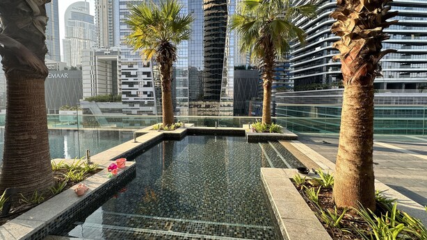 Un cadre urbain moderne avec une fontaine centrale, entourée de palmiers et d’une piscine.