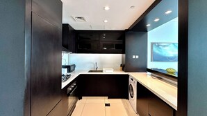 Une cuisine moderne avec des meubles de rangement de couleur sombre, un four à micro-ondes encastré, un évier et un lave-linge.