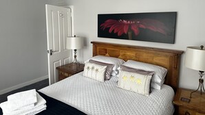A neatly arranged bedroom with a bed, bedside lamps, a door, and a wall-mounted flower painting. - The Sandgate New Immaculate 1-bed Apartment in Ayr (Ayr)