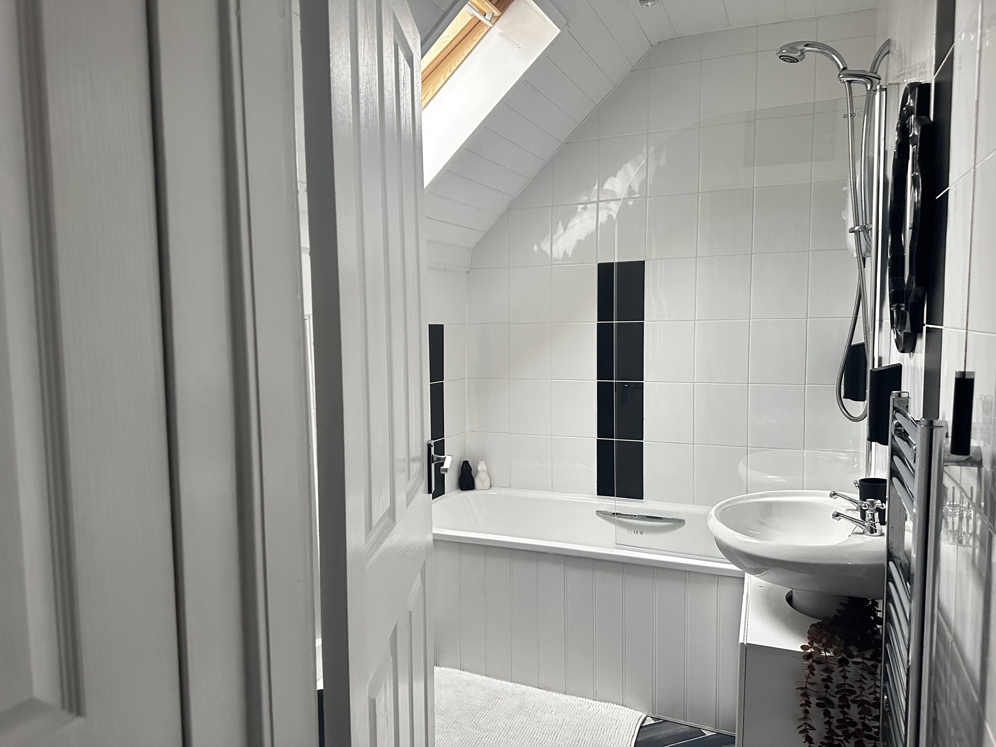 Une salle de bain moderne avec des carreaux blancs, un puits de lumière, une baignoire et un lavabo.