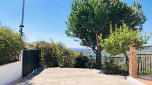 Ein gepflasterter Patio-Bereich mit einem Metallzaun, einem großen Baum und Blick auf die Landschaft.