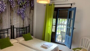 Ein Zimmer mit zwei Betten, einem Fenster mit blauer Tür, einem grünen Vorhang und einem weißen Stuhl mit Lampe.