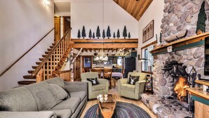 A cozy living room with a stone fireplace, wooden staircase, and a dining area. - Stepaway Vacation Rentals - Shimmering Waters (St. Germain)