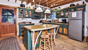 A kitchen with wooden cabinets, a central island, bar stools, a refrigerator, and hanging pendant lights. - Stepaway Vacation Rentals - Shimmering Waters (St. Germain)