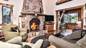 A cozy living room with a stone fireplace, comfortable seating, and a large window offering a view of the outdoors. - Stepaway Vacation Rentals - Shimmering Waters (St. Germain)