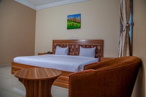 A hotel room with a large bed, a wooden side table, and two upholstered chairs.
