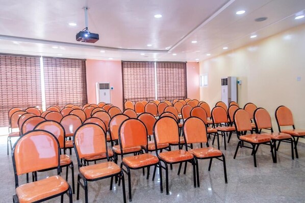 A conference room with rows of orange chairs, a projector, and air conditioning units.
