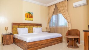 A bedroom with a wooden bed, a nightstand, a chair, and a painting on the wall. - Guest Pride Hotel Kano  (Kano)