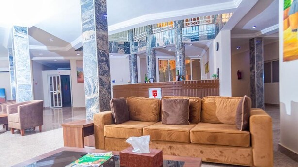 A lobby with a brown sofa, a glass coffee table, and a reception desk. - Guest Pride Hotel Kano  (Kano)
