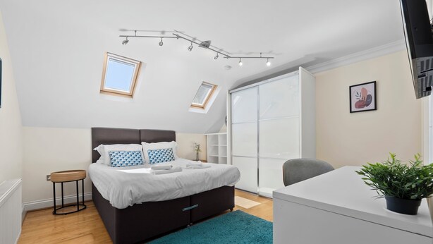 Ein modernes Schlafzimmer mit Bett, Schreibtisch, Stuhl, einem kleinen Tisch und einem Blumentopf.