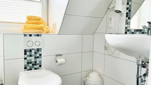 A bathroom with a toilet, sink, and a towel rack with folded towels. - Haus Möwe App Austernfischer Westerland (Westerland)