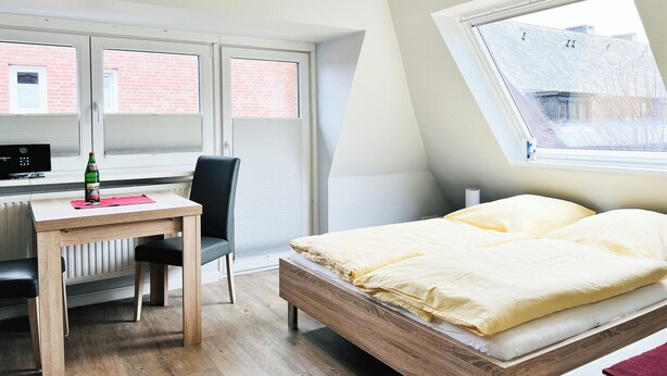 A bedroom with a wooden bed, a desk with a chair, and a window with a view of a brick building. - Haus Möwe App Austernfischer Westerland (Westerland)