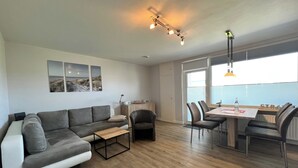 A modern living room with a grey sofa, a wooden coffee table, and a dining area with a table and chairs. - App Sylter Welle Westerland (Westerland)