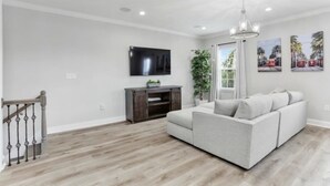A modern living room with a grey sofa, wooden flooring, a flat-screen TV, and a dark wooden cabinet. - Pleasant Peachy Escape (New Orleans)
