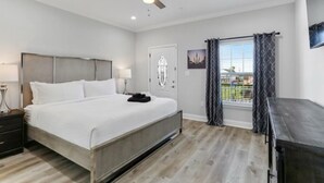 A bedroom with a bed, nightstands, a ceiling fan, a window with curtains, and a door with a decorative glass panel. - Pleasant Peachy Escape (New Orleans)