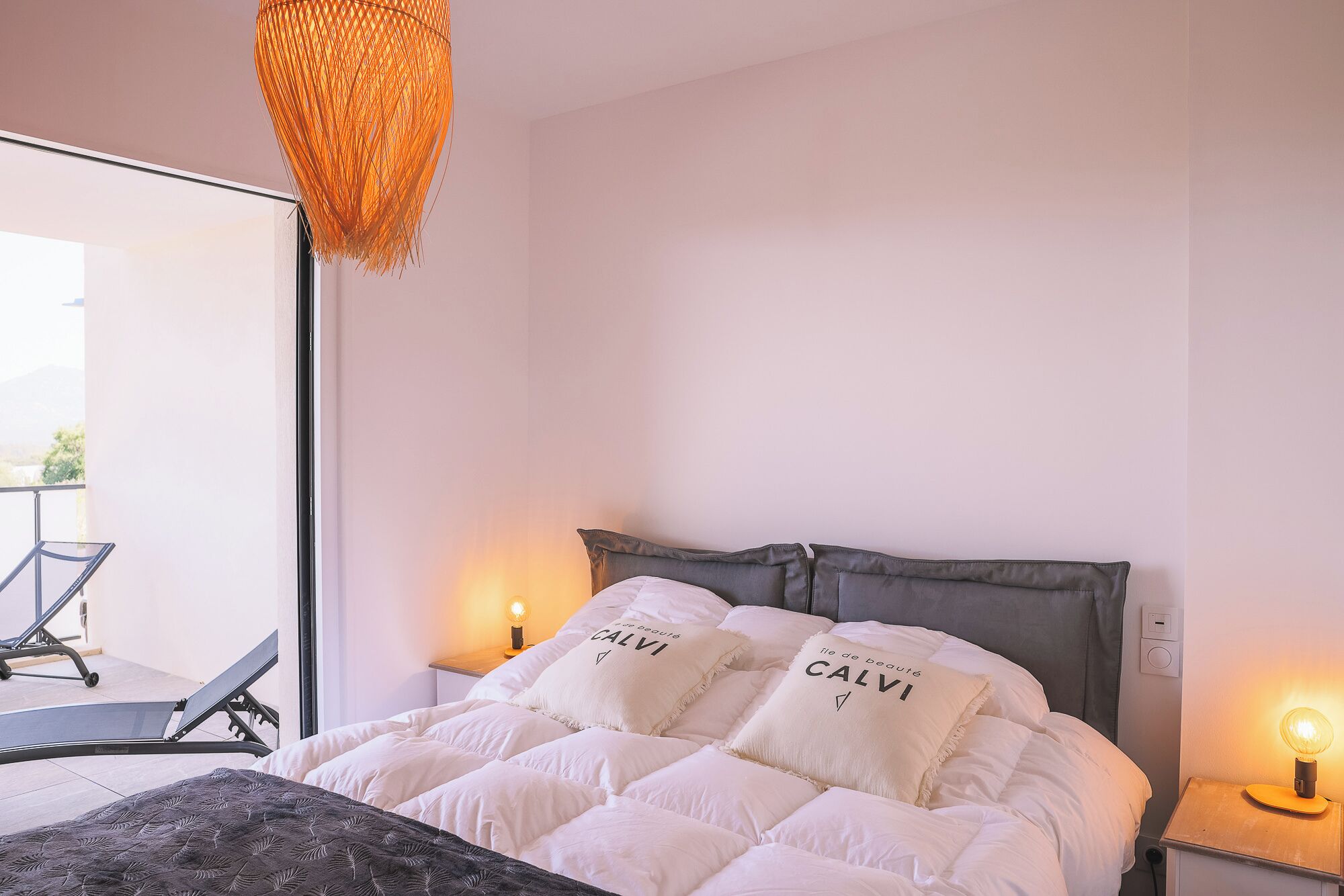 A bedroom with a bed, two bedside lamps, and a hanging light fixture.