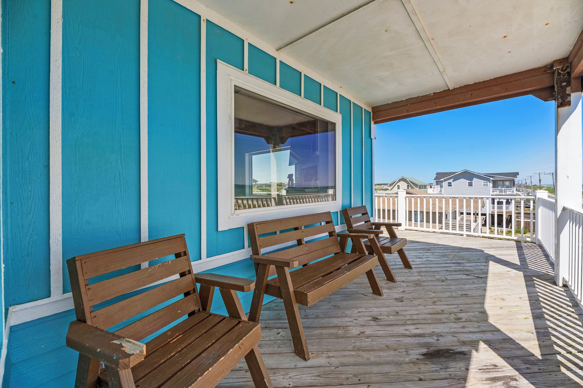 A wooden deck with benches, a window, and a view of houses in the background.
