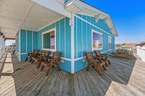 A covered outdoor seating area with wooden chairs and tables, a blue and white building, and a wooden deck. - Mariposa: Ocean Views, Private Pool, Putting Green (Kitty Hawk)