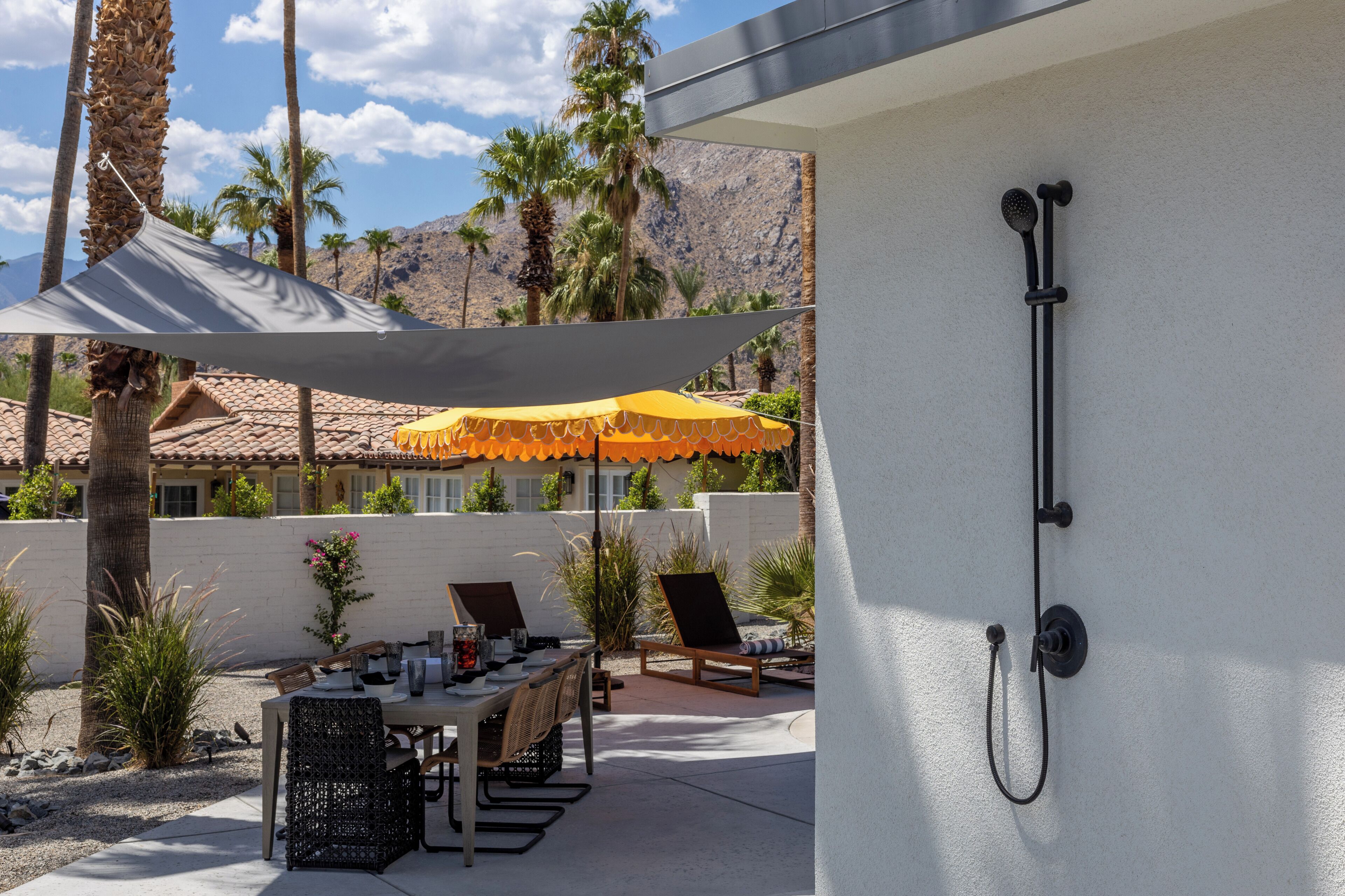A patio with a table and chairs, a yellow umbrella, and a shower area.