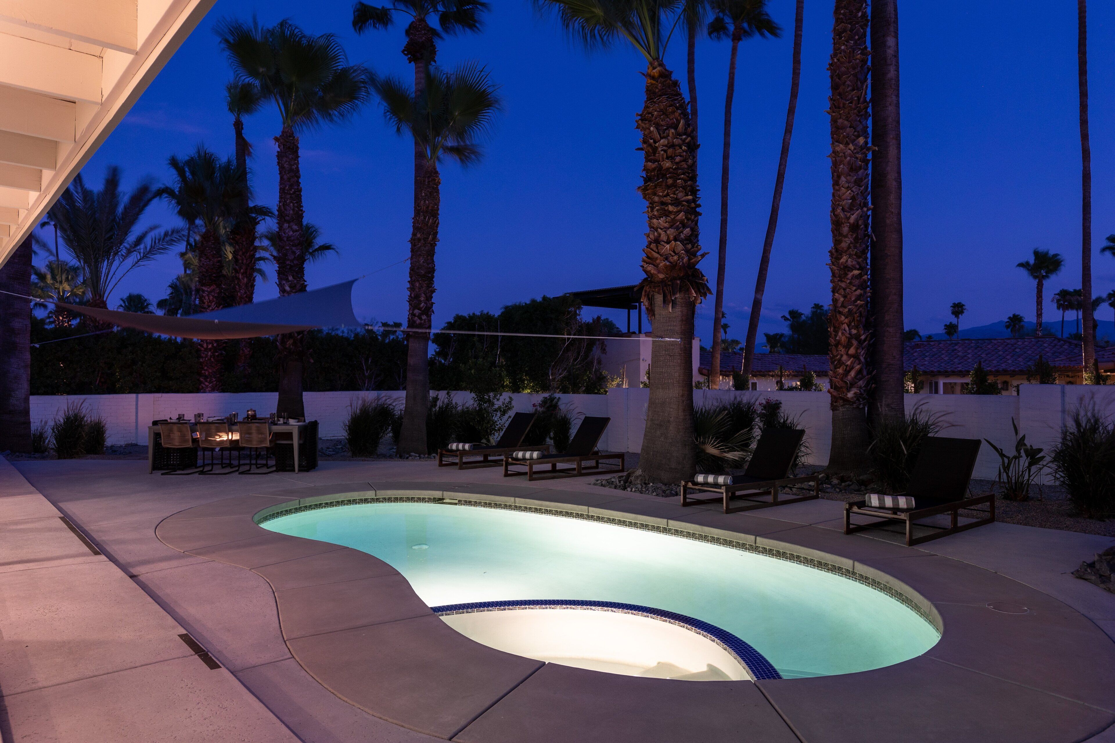 A swimming pool with lounge chairs and a table, surrounded by palm trees.